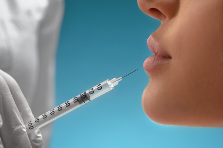 Agulha em boca feminina fazendo preenchimento labial com ácido hialurônico.