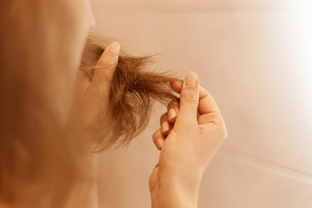 Mulher com a mão nas pontas do cabelo ruivo com as pontas mal cuidadas.